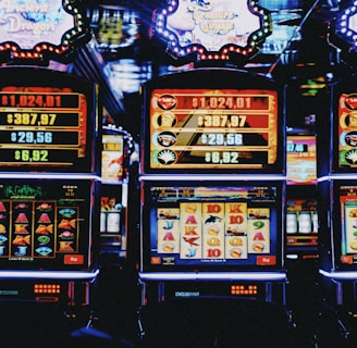 A row of colorful slot machines lit with bright neon lights, showcasing various graphical elements on the screens, indicating different games and jackpots. The atmosphere suggests a lively casino setting, bustling with excitement.