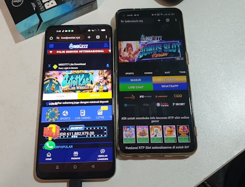 Two smartphones are displayed on a white surface, both showing gambling websites with colorful graphics, text, and various options for logging in and accessing games. The screens are bright and filled with promotional content related to casino and slot games.